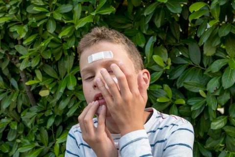 Boy with plaster on his face in front of a hedge looks sad Stock Photos
