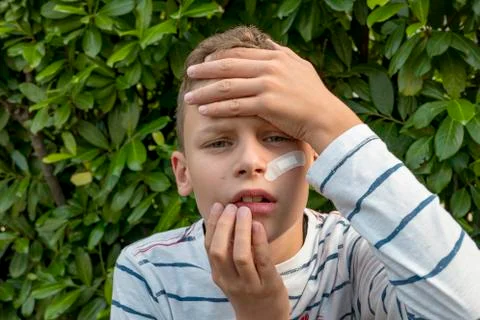 Boy with plaster on his face in front of a hedge looks sad Stock Photos