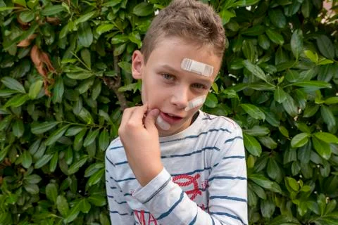 Boy with plaster on his face in front of a hedge looks sad Foto stock