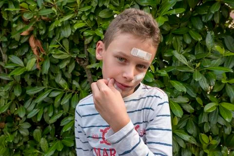 Boy with plaster on his face in front of a hedge looks sad Stock Photos