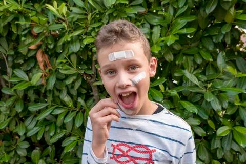 Boy with plaster on his face in front of a hedge looks sad Stock Photos