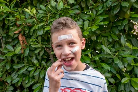 Boy with plaster on his face in front of a hedge looks sad Stock Photos