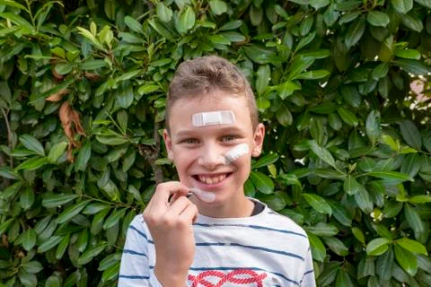 Boy with plaster on his face in front of a hedge looks sad Stock Photos