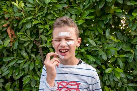 Boy with plaster on his face in front of a hedge looks sad Stock Photos