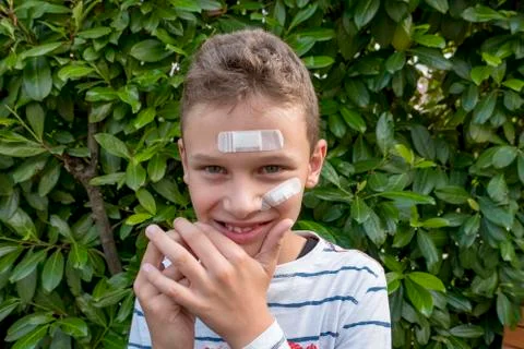 Boy with plaster on his face in front of a hedge looks sad Stock-Fotos