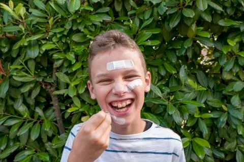 Boy with plaster on his face in front of a hedge laughing Stock Photos