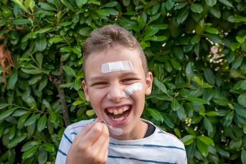 Boy with plaster on his face in front of a hedge laughing Stock Photos
