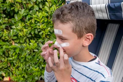 Boy with plaster on his face in front of a hedge laughing Stock Photos