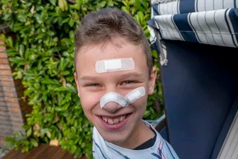 Boy with plaster on his face in front of a hedge laughing Stock Photos