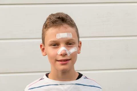 Boy with plaster on his face in front of a hedge laughing 스톡 사진