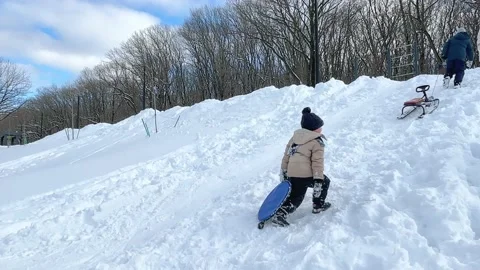 Boy with plastic board in hand trying to get to the top of snow hill to slide Stock Footage 232992578