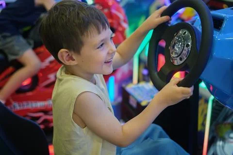 Boy playing arcade racing game in entertainment center. Child smiling while d Stock Photos