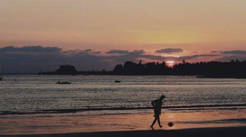 A boy playing with ball on a beach during sunset. Stock Photos