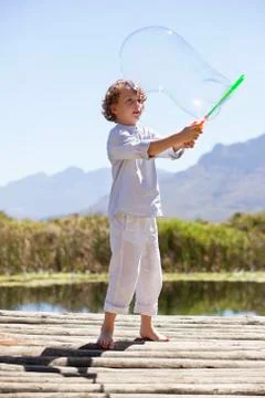 Boy playing with a bubble wand at a pier Stock Photos