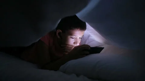Boy playing with a cellphone or smartphone on a bed. hiding under a blanket Stock Footage