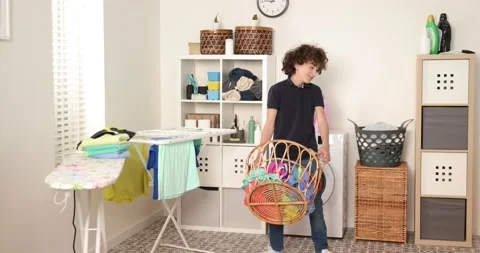 Boy is playing with clothes during laundry. Young teen boy throwing basket with Stock Footage 178541953