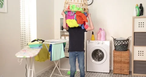 Boy is playing with clothes during laundry. Young teen boy throwing basket with Stock Footage 178544692