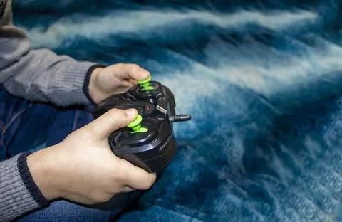 The boy is playing a computer game. Black joystick in hands on a pastel blu.. Stock Photos