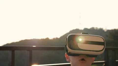 The boy is playing on the computer in virtual reality glasses in the sunset at 库存影片 94556437