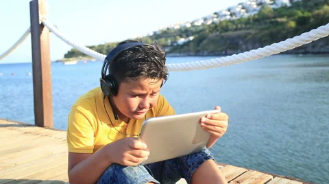 Boy playing digital tablet  computer on wooden pier by the sea 2 Video stock 64786933
