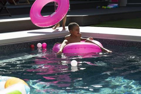 Boy playing, floating in inflatable ring in sunny, summer swimming pool Stock Photos