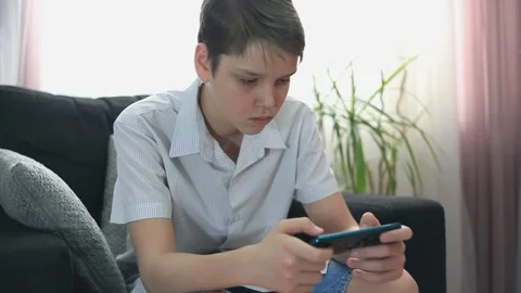 Boy Is Playing A Game On His Phone. Teenager Plays in a Smartphone Stock Footage 153319842