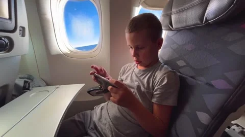 A boy is playing a game on his smartphone, sitting in the cabin of an airplane Stock Footage 314094230