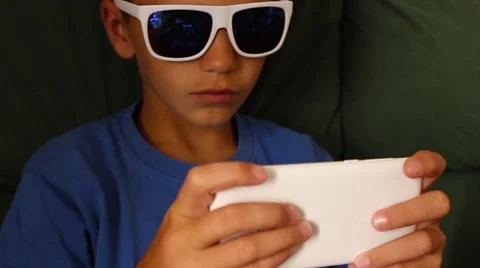 Boy playing games on your mobile phone in dark glasses Stock Footage 65300434