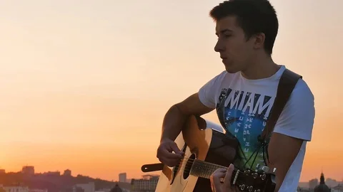 Boy playing guitar on evening sunset background Stock Footage 107940755