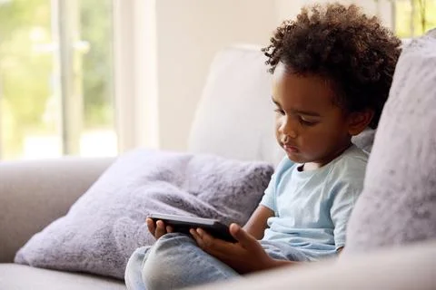 Boy Playing Handheld Computer Game Sitting On Sofa At Home Stock Photos