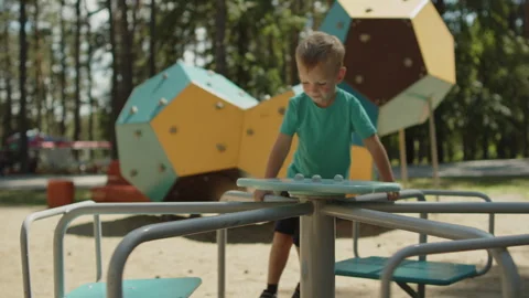 Boy playing on a merry-go-round carousel at a sunny public playground. Video stock 343207658