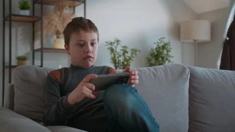 Boy Playing Mobile Game on Couch. Focused child digital fun relaxed home leisure Stock Footage 335480440