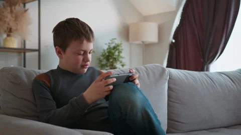 Boy Playing Mobile Game on Sofa. Focused child digital leisure cozy home Stock Footage 335480635