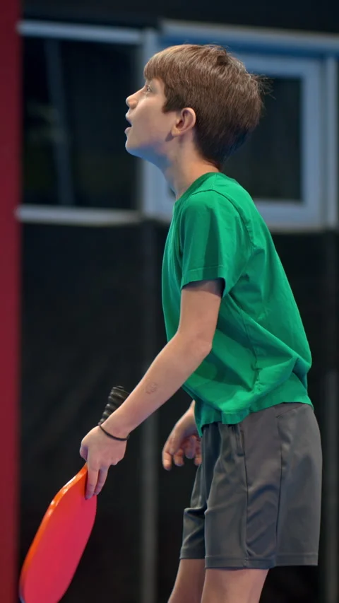 A boy playing pickleball on a blue, inside court. Vertical Stock Footage 297513054