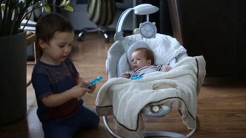Boy playing with a plastic toy next to his newborn brother Stock Footage 84490351