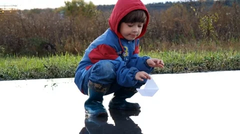 Boy playing in puddle with paper ship 스톡 동영상 45924517