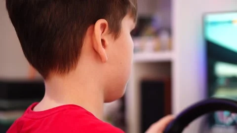 Boy playing racing simulator on computer steering wheel rear view Stock Footage 297450906