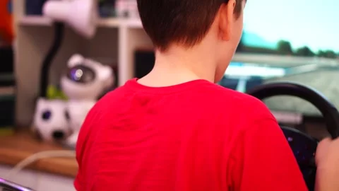 Boy playing racing simulator on computer steering wheel rear view Stock Footage 297450947
