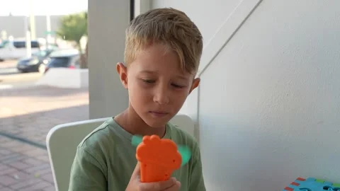 Boy Playing with Small Orange Handheld Electric Fan Indoors Stockbeeldmateriaal 345170978