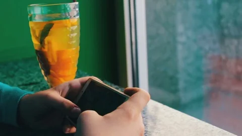 A boy playing on a smartphone in a cafe next to lemon tea with cinnamon Stock Footage