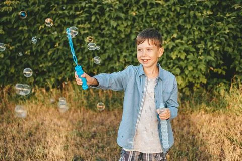 A boy is playing with soap bubbles in a summer park, Among the greenery. Stock Photos
