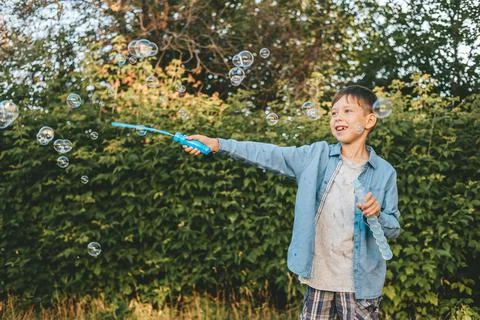 A boy is playing with soap bubbles in a summer park, Among the greenery. Stock Photos