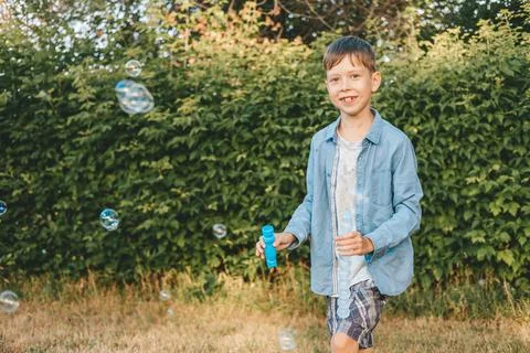 A boy is playing with soap bubbles in a summer park, Among the greenery. Stock Photos