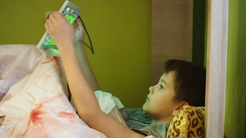 Boy playing tablet lying under a blanket in bed Stock Footage 144045582