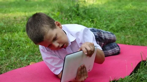A boy is playing in a tablet in the park Stock Footage 92153411