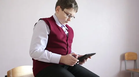 Boy playing tablet sitting on the desk in the classroom Stock Footage 58866845