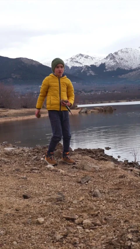Boy playing throwing stones into a lake with snowy mountains in the backgro.. Stock Footage 261816354