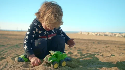 The boy is playing with a toy green dump truck on the beach 動画素材 76011718