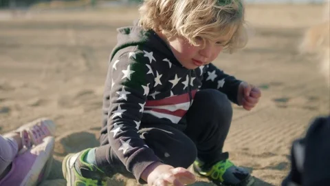 The boy is playing with a toy green dump truck on the beach 動画素材 76014214