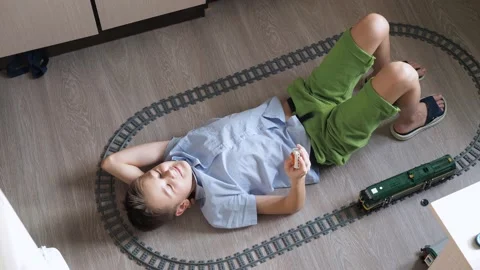 A boy is playing with a train on the controls on the floor in the room. top view Stock Footage 170446211